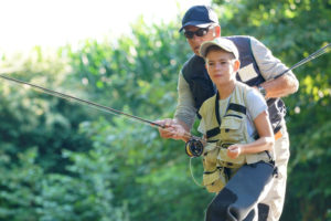 Young man learning to fly fish with older man.